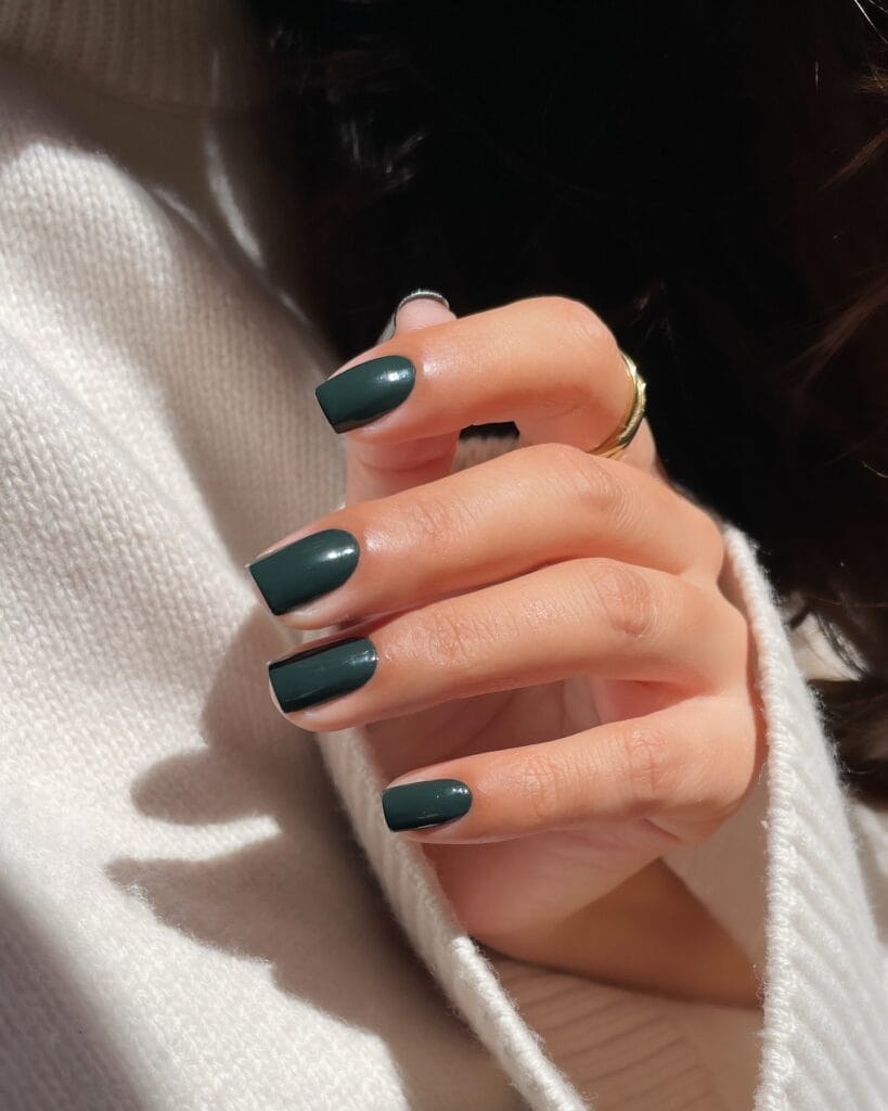Short square forest green nails with a high-gloss finish in sunlight, fall nails inspiration.