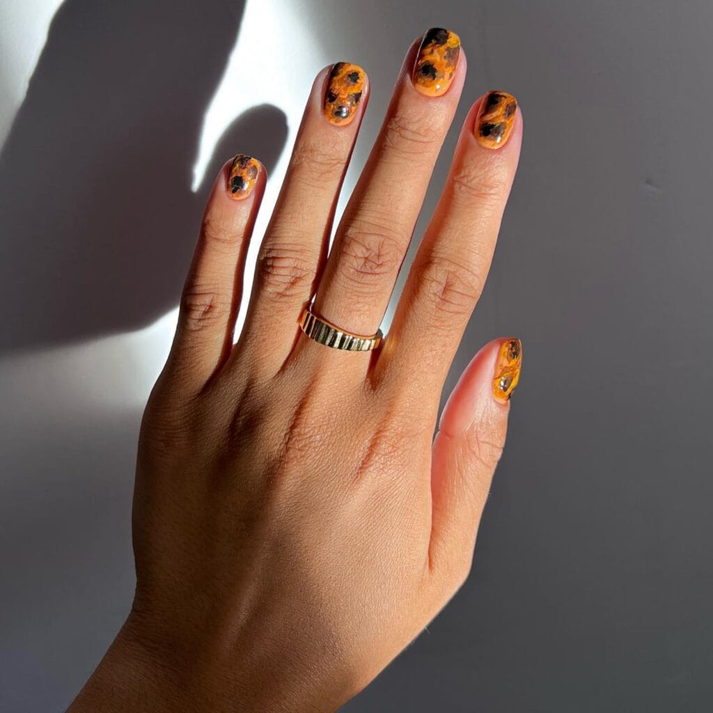 Short tortoiseshell nails with bright amber-orange and black irregular patches.
