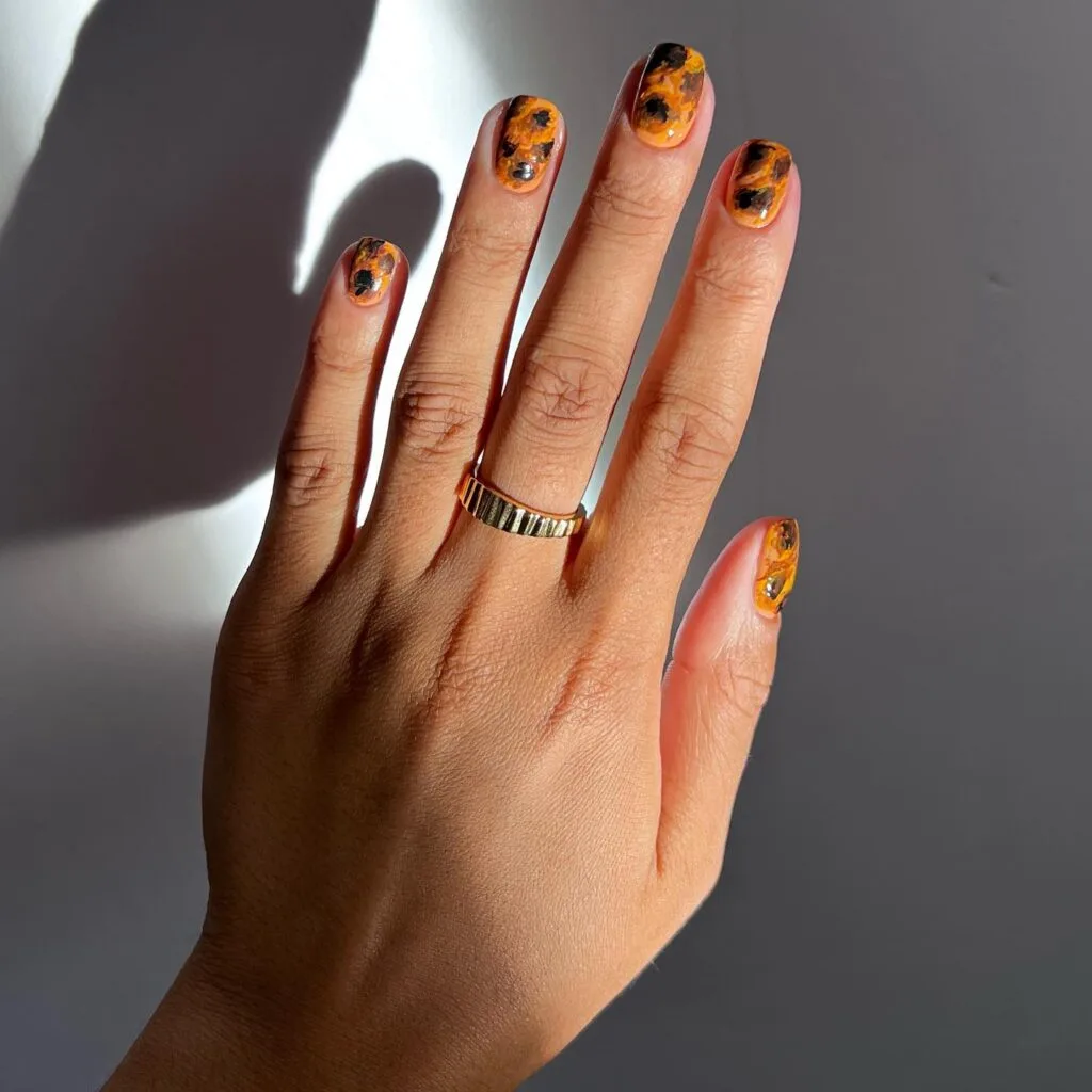 Short tortoiseshell nails with bright amber-orange and black irregular patches.
