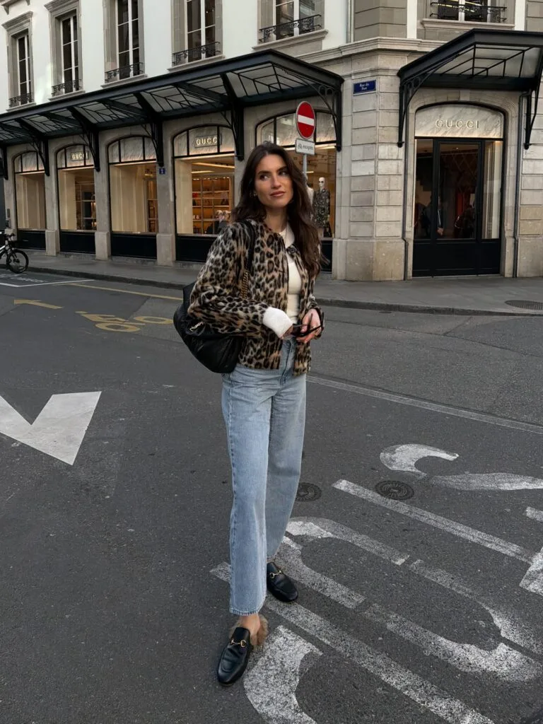 Woman in a leopard-print jacket, straight-leg jeans, and loafers in a fall 2026 outfit on a city street.