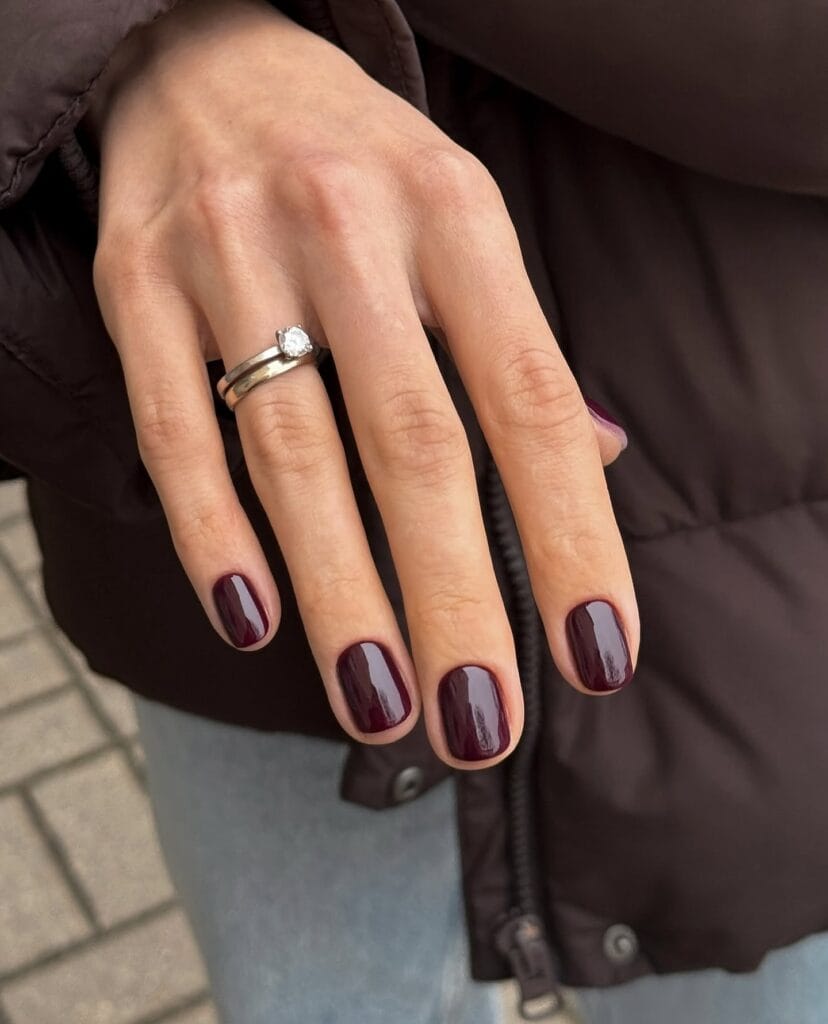 Short glossy black cherry nails on a natural square shape with a silver ring, fall nails inspiration.