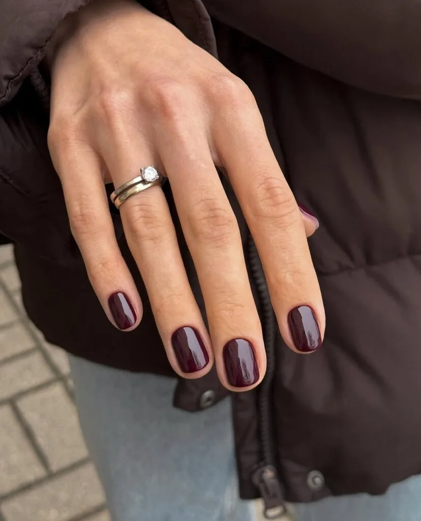 Short glossy black cherry nails on a natural square shape with a silver ring, fall nails inspiration.