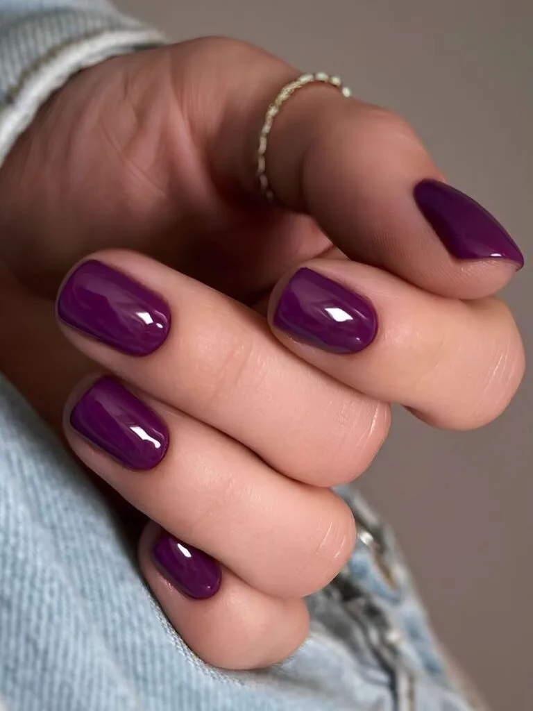 Short rounded sugar plum nails in deep glossy purple, an autumn nail colors idea.