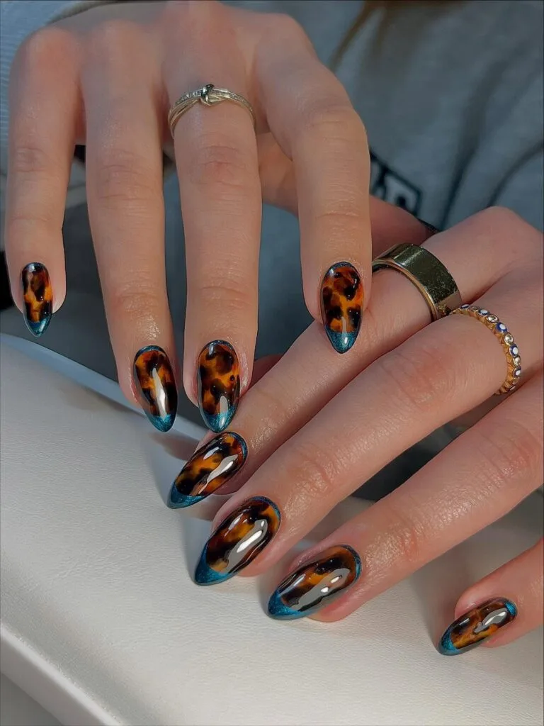 Almond tortoise shell nails with glossy amber pattern and metallic teal French tips.
