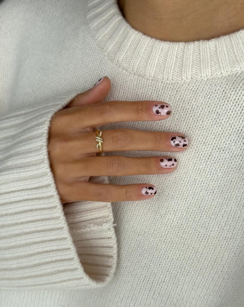 Short blush autumn nails with irregular chocolate brown cow-print spots.