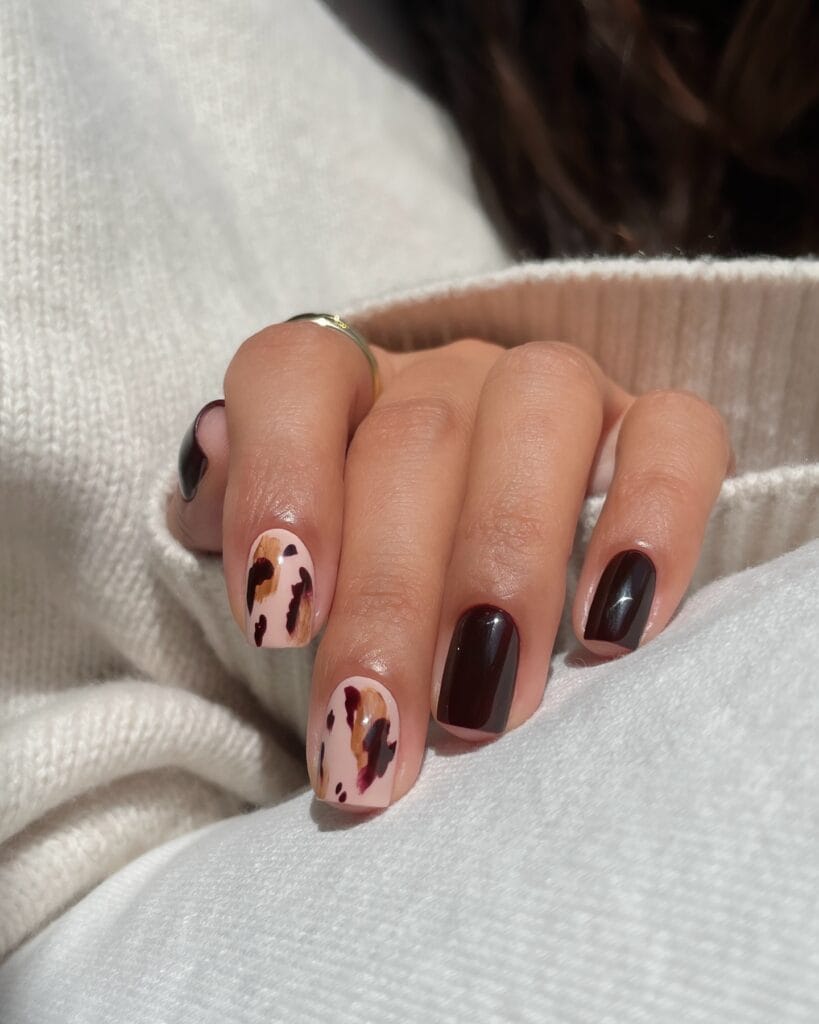 Short September nails with dark burgundy polish and abstract brown brushstroke accents.