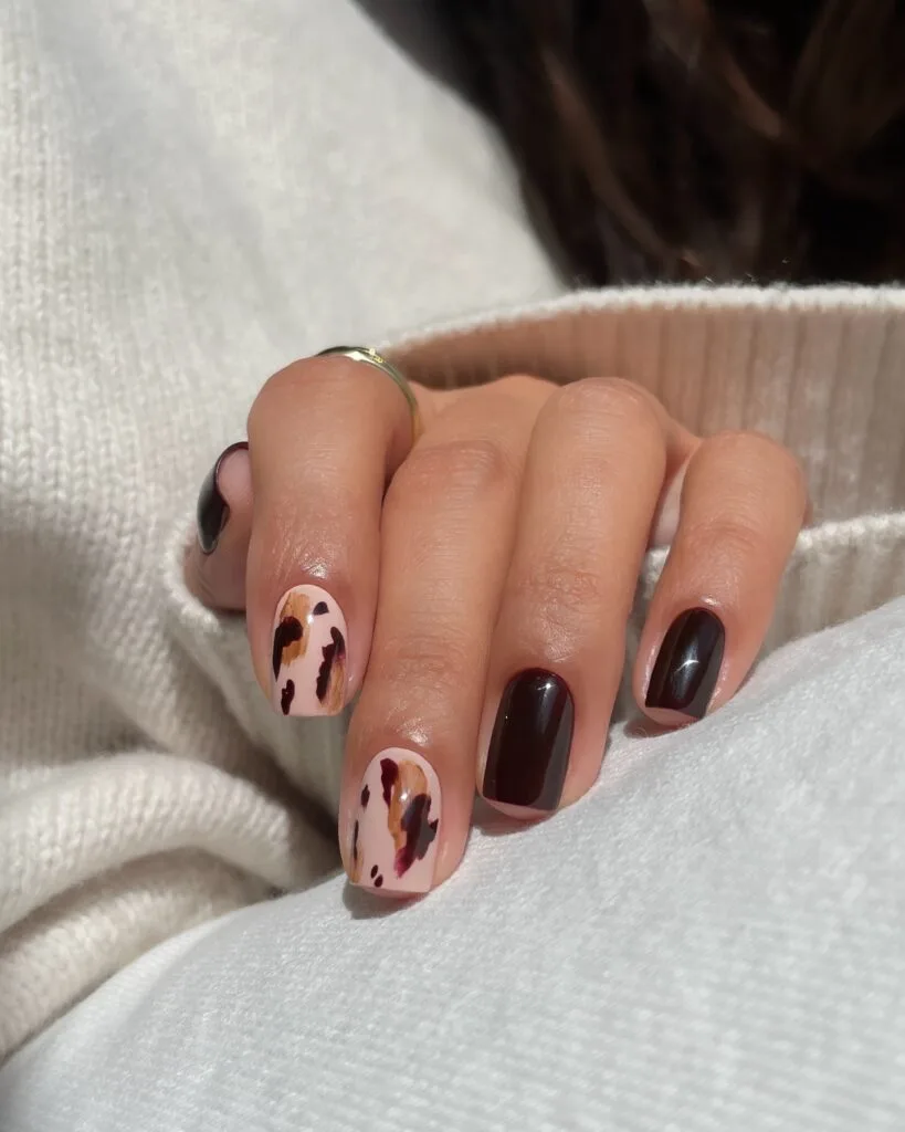 Short September nails with dark burgundy polish and abstract brown brushstroke accents.