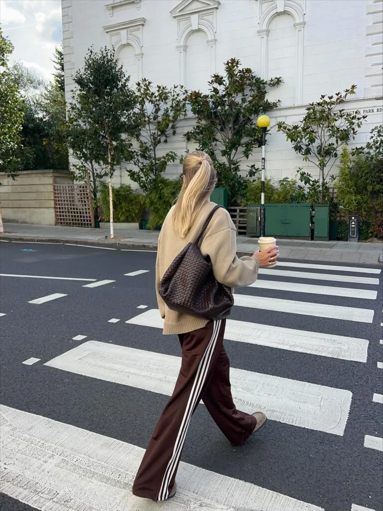 Woman in burgundy track pants with a beige sweater and white shirt in a casual fall outfit.