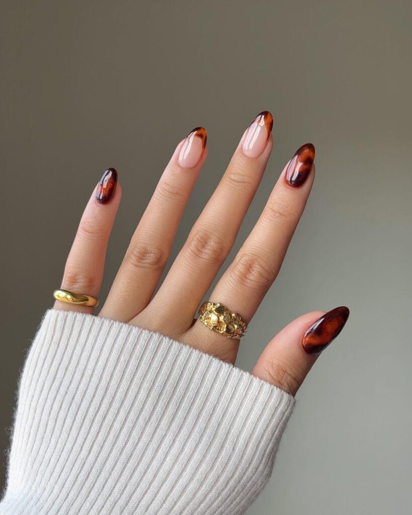 Sheer pink almond nails with tortoiseshell French tips and full amber-brown accent nails.
