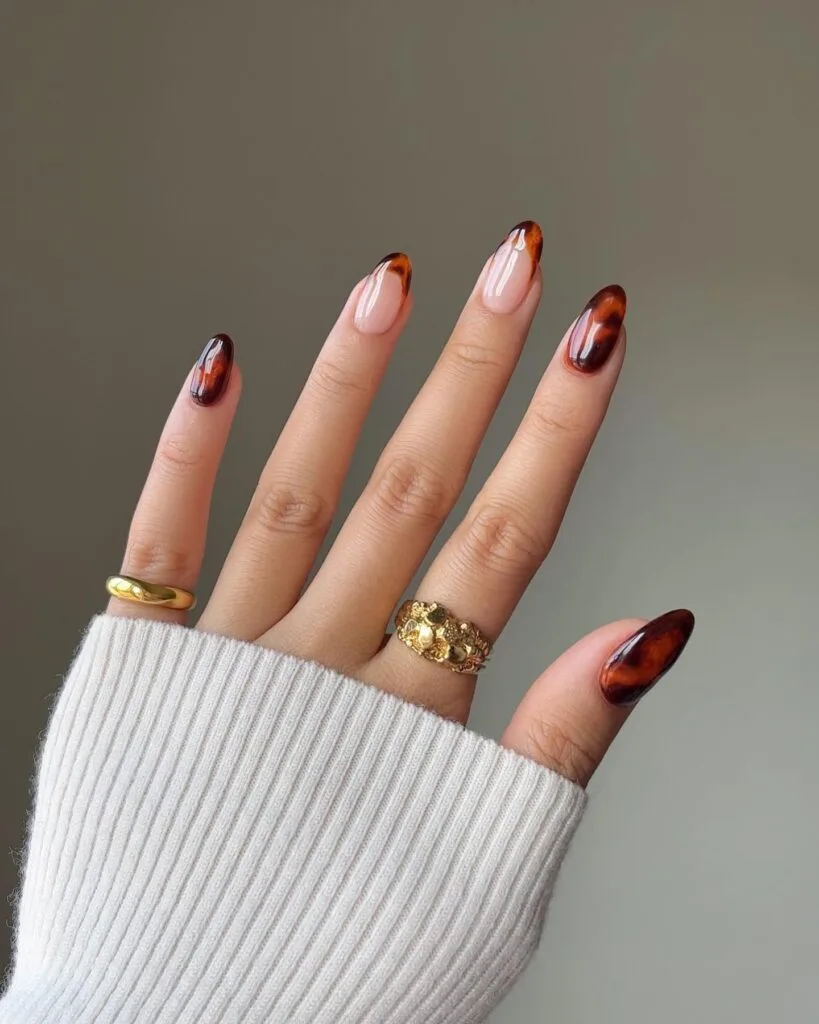 Sheer pink almond nails with tortoiseshell French tips and full amber-brown accent nails.

