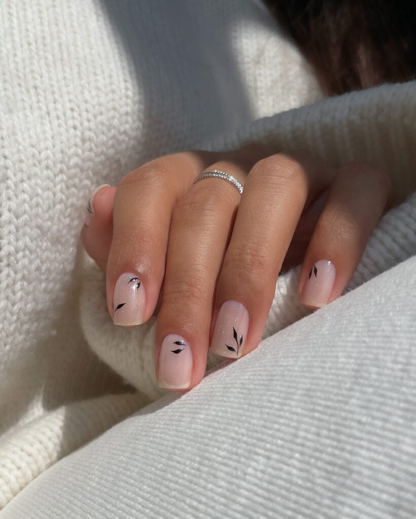 Short neutral fall nails with sheer pink shimmer, pale tips, and tiny black leaf accents.
