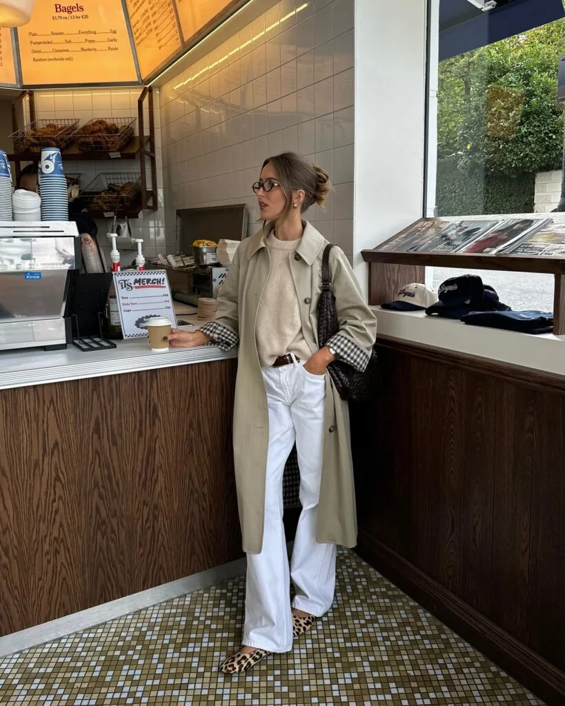 Fall fashion outfit with trench coat, beige sweater, white jeans, and leopard flats.