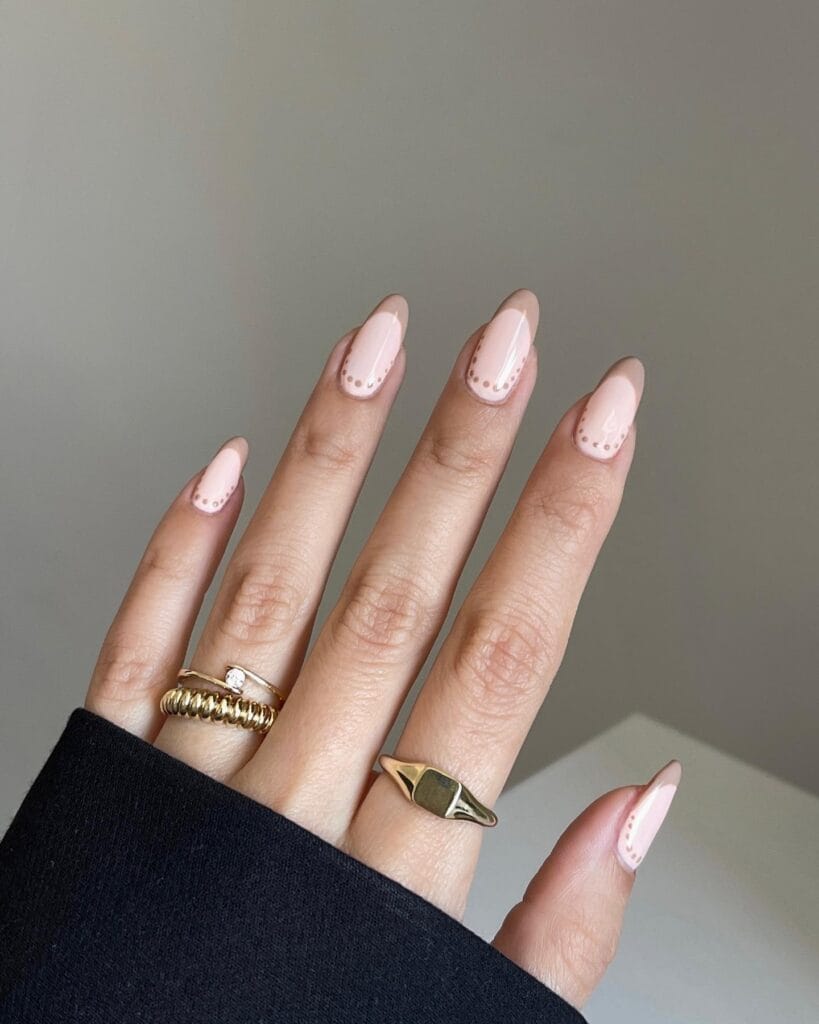 Pale pink nude almond nails with beige French details and tiny dotted accents.
