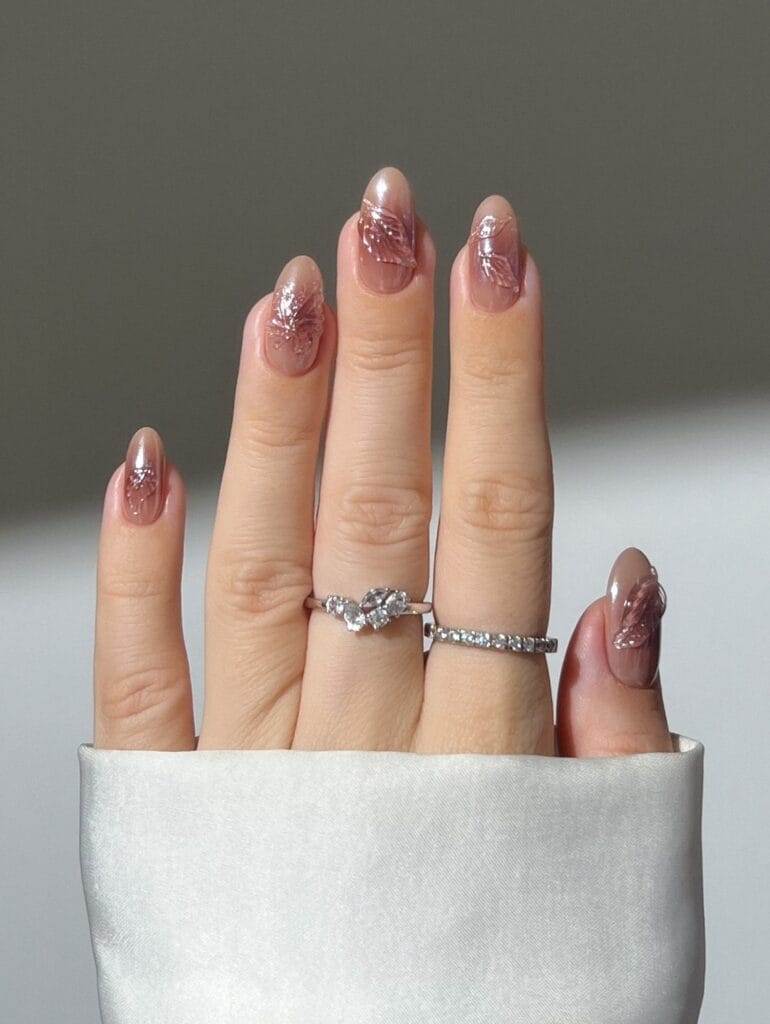 Taupe neutral fall nails with raised translucent rose-pink leaf accents and a glossy finish.