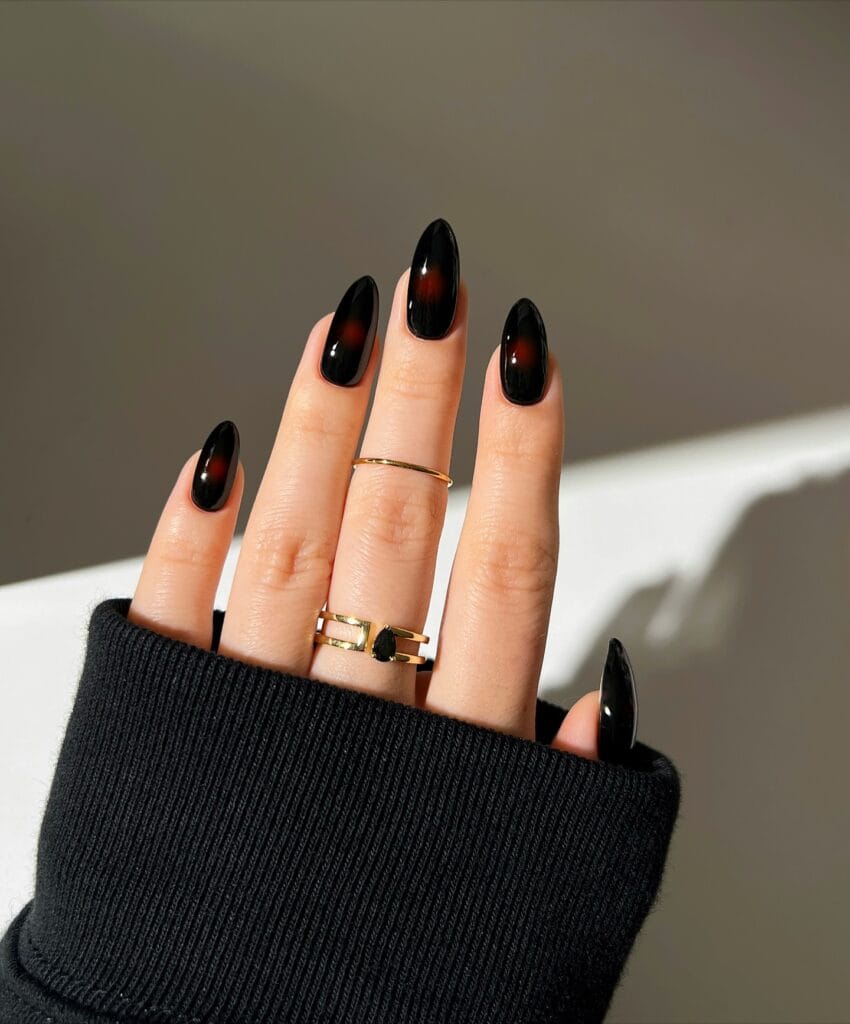 Glossy black autumn nails with small diffused red aura centers on almond shapes.
