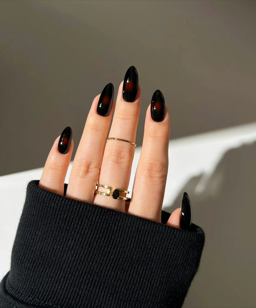 Glossy black autumn nails with small diffused red aura centers on almond shapes.