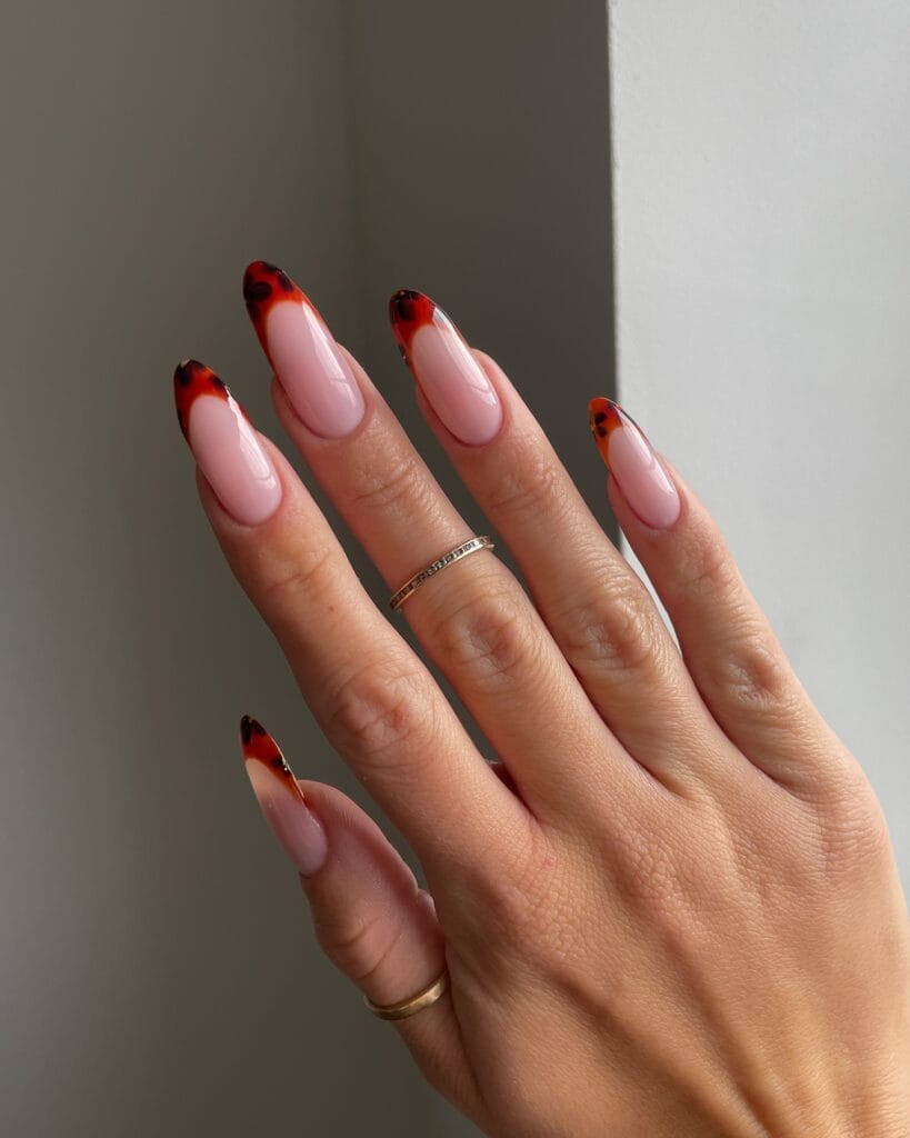 Long almond nails with translucent red-orange tortoiseshell French tips over a milky pink base.

