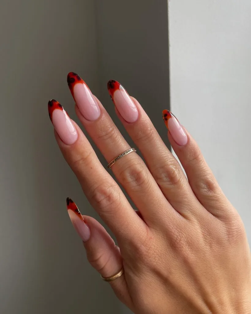 Long almond nails with translucent red-orange tortoiseshell French tips over a milky pink base.
