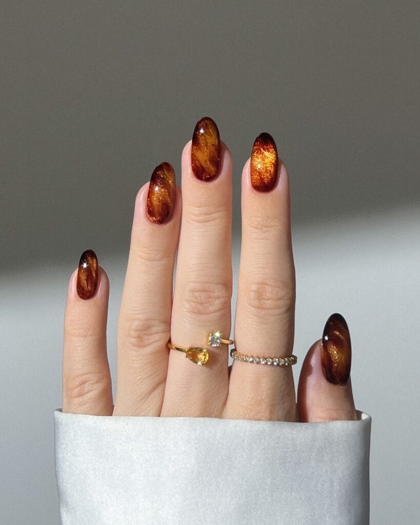 Glowing copper almond nails with dark edges and metallic shimmer, a fall nail colors look.