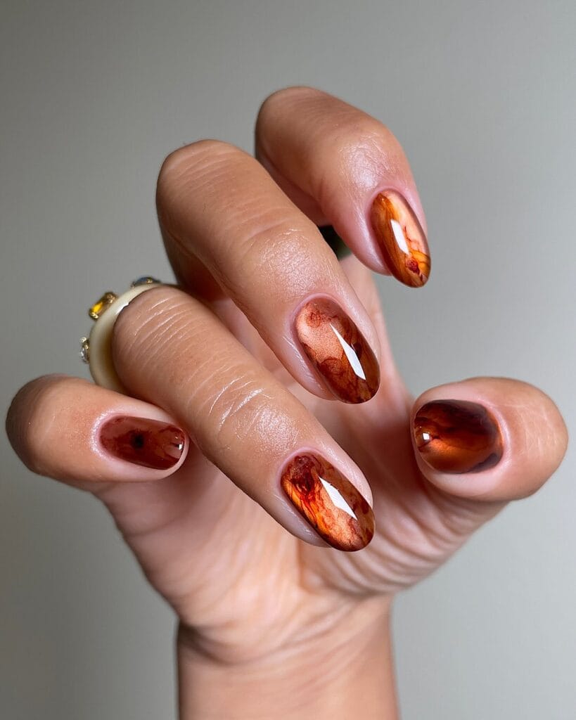 Glossy mirrored copper oval nails with molten amber swirls, an autumn nails idea.
