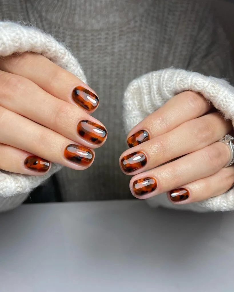 Short square tortoiseshell nails with glossy amber and dark brown irregular patches.
