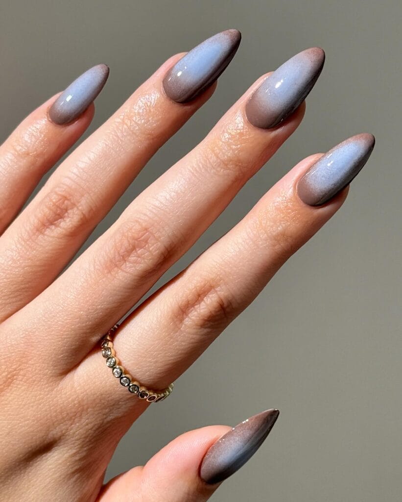 Pale blue fall aura nails with smoky taupe-grey edges and glossy almond shapes.
