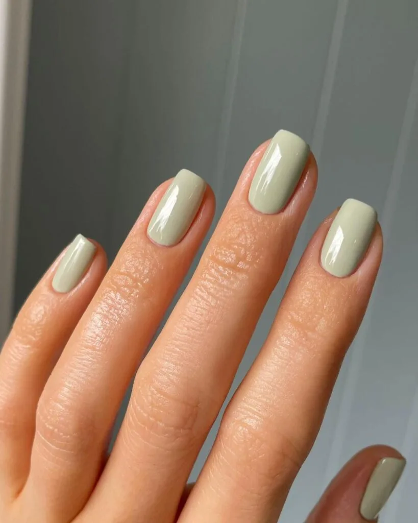 Short square glossy sage green nails in a pale muted shade for September nails.