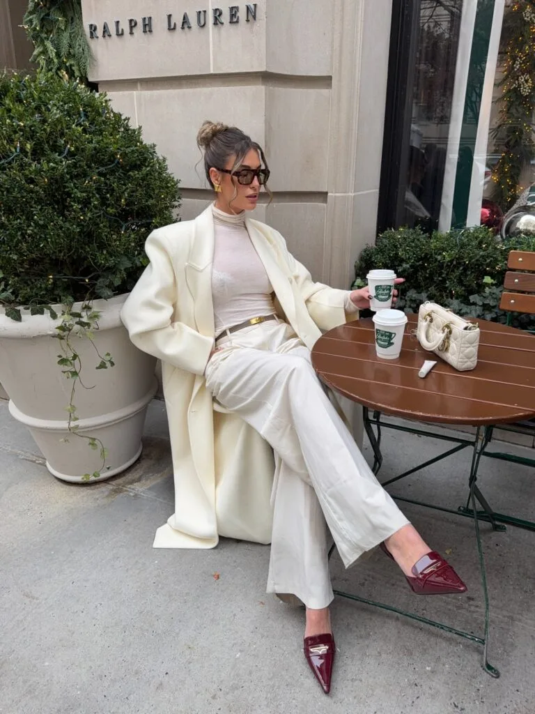 Woman in a cream coat and ivory trousers with burgundy loafers in an autumn outfit.