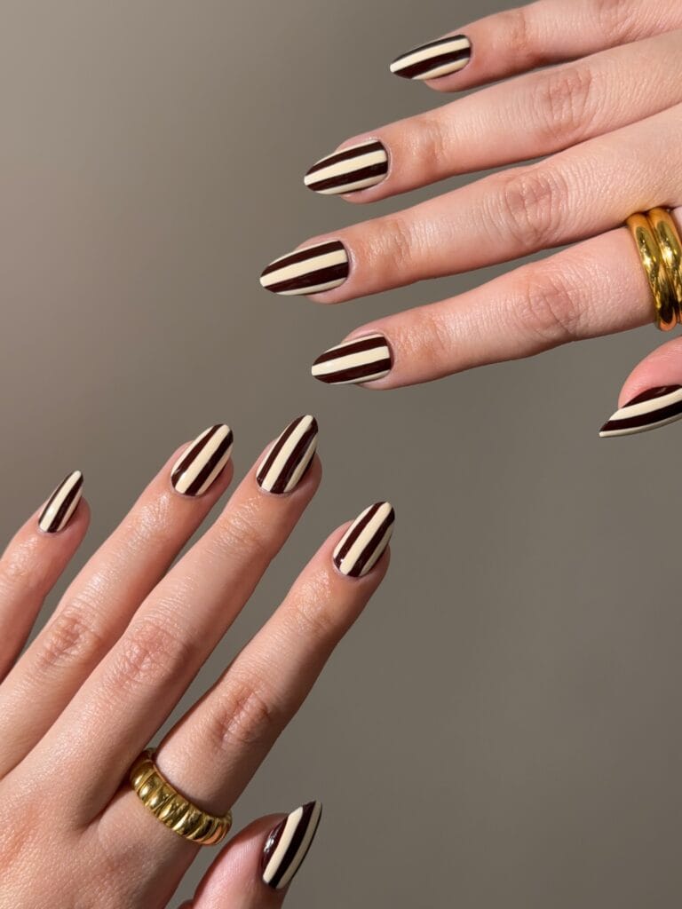 Almond autumn nails 2026 with bold chocolate brown and cream vertical stripes