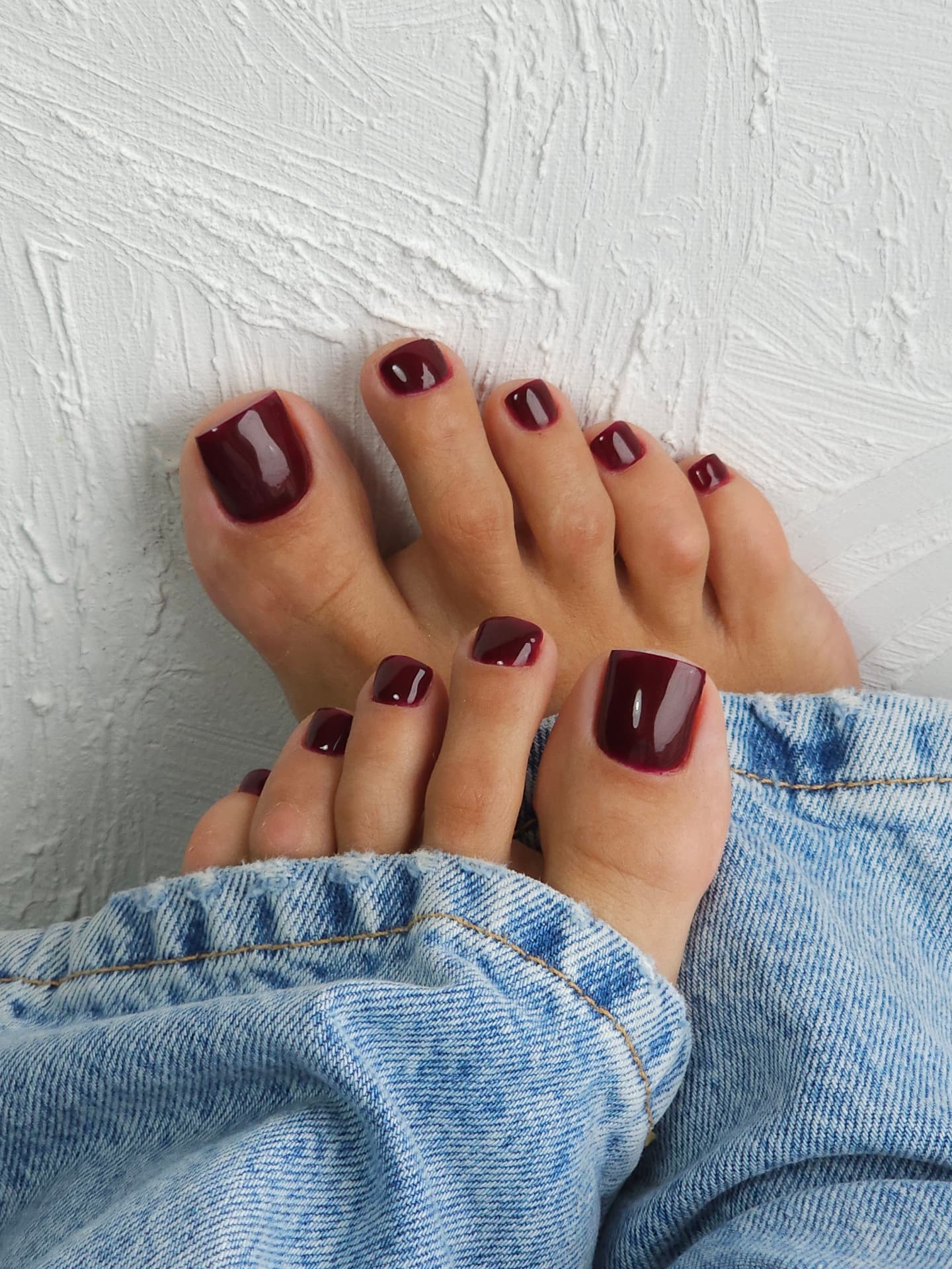 Glossy black cherry fall pedicure with short square toenails and light blue jeans.