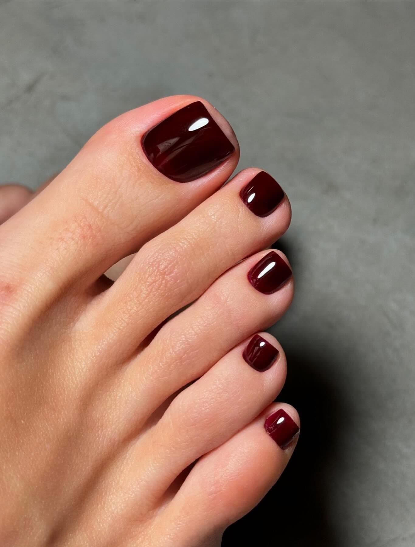 Deep burgundy toe nail color for fall with a glossy finish on short, squared nails.
