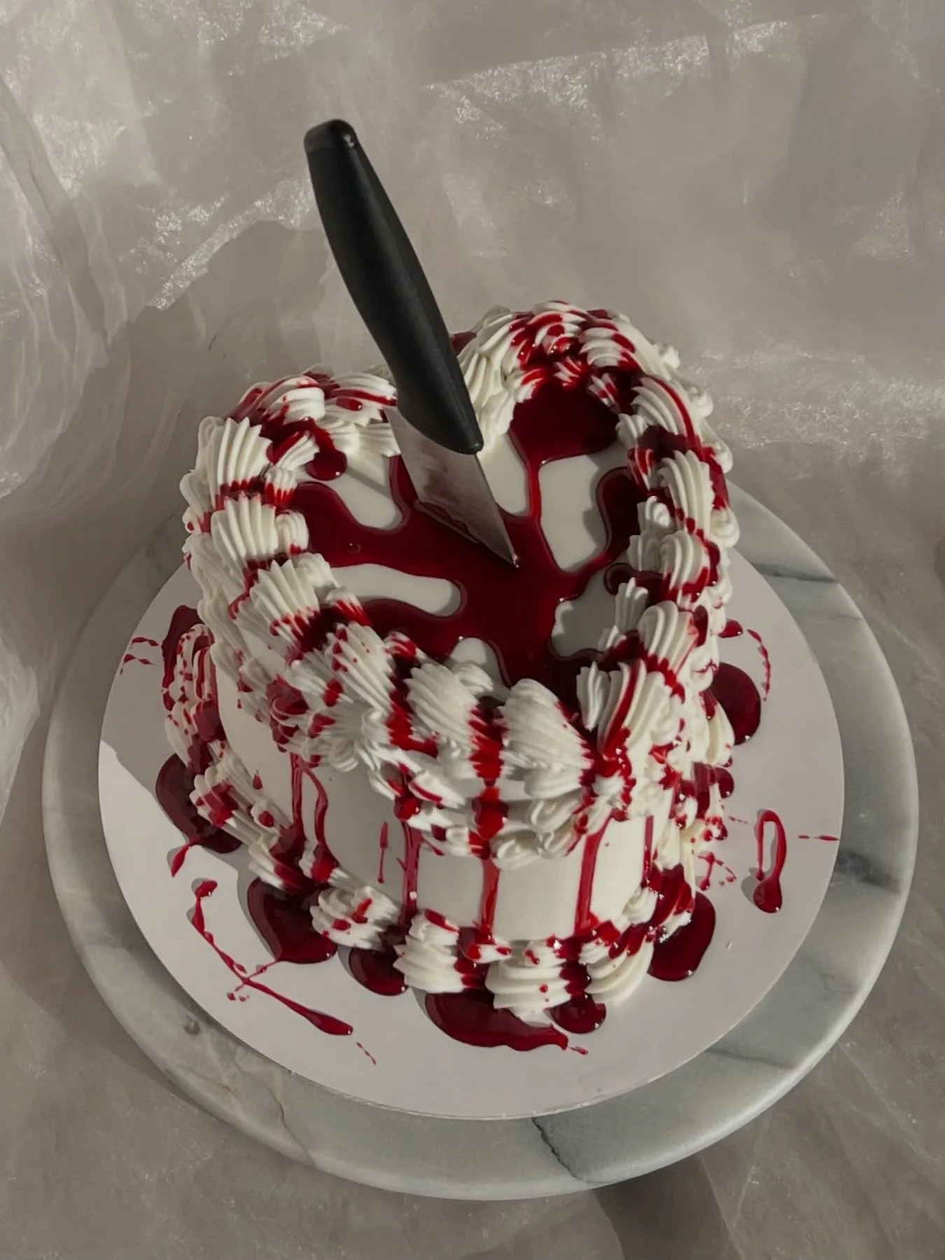 Halloween cake with white frosting, red drip icing, and a knife pressed into the center
