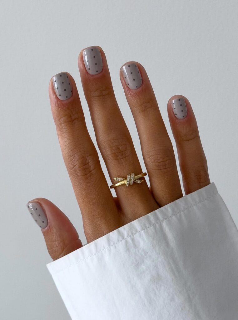 Short, softly squared autumn nails with a glossy light gray base and tiny darker gray polka dots.
