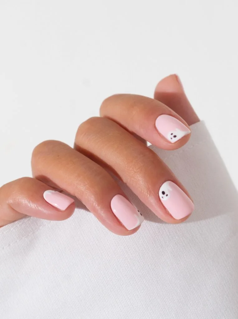 short Halloween nails in soft pink with tiny white ghost accents peeking from the corners