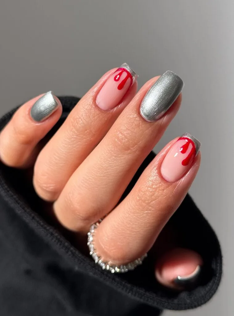 short Halloween nails with silver chrome polish and red drip accents over a nude base