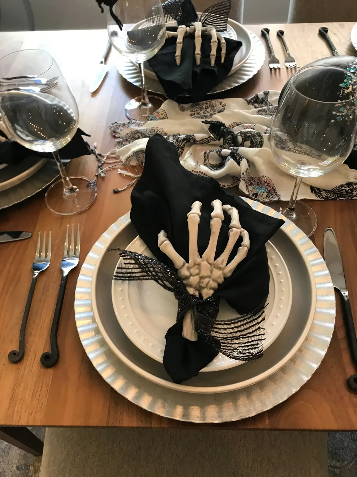 Halloween place setting with a skeleton hand tied over a black napkin on silver plates
