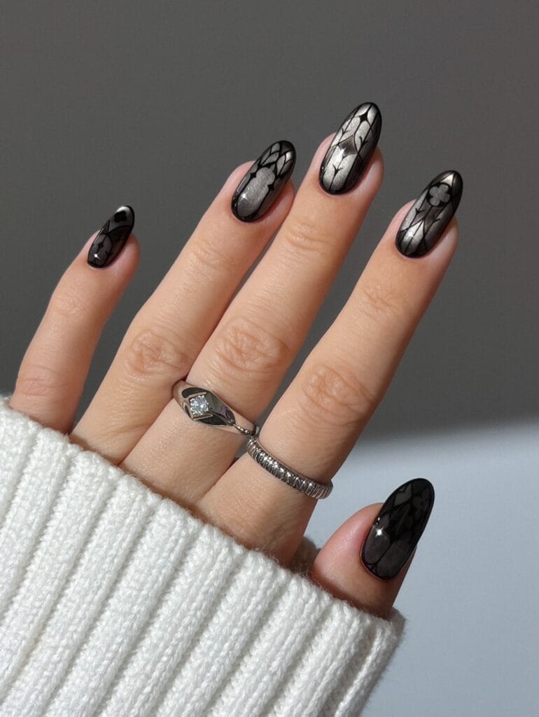 Silver and black witchy nails with fine Gothic window outlines and dark borders on oval shapes.