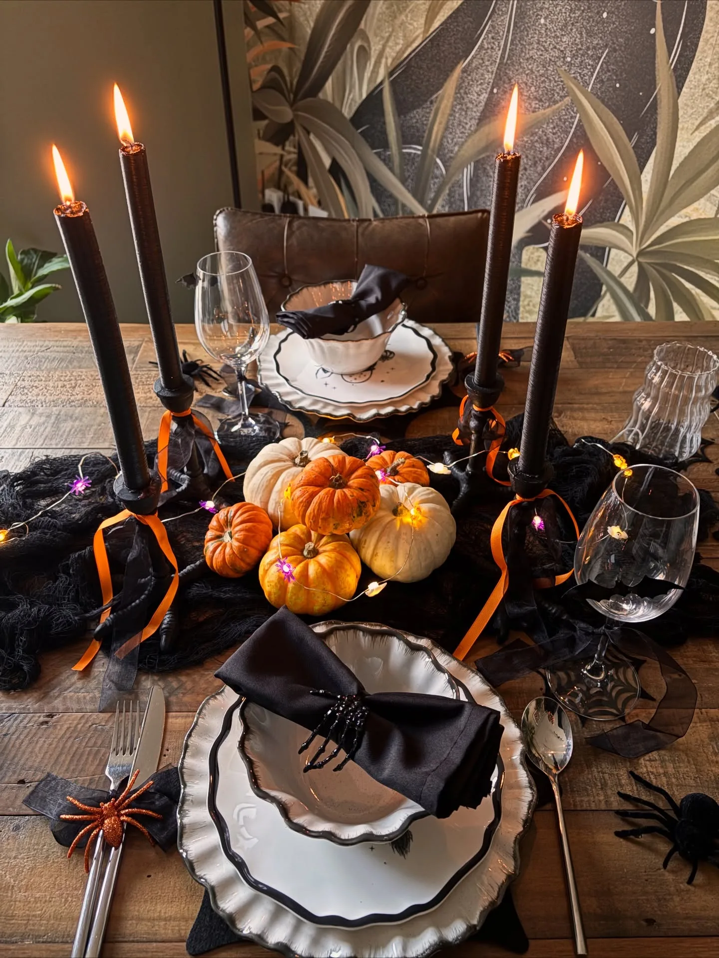 Halloween tablescape with black candles, pumpkins, spider details, black napkins, and white plates
