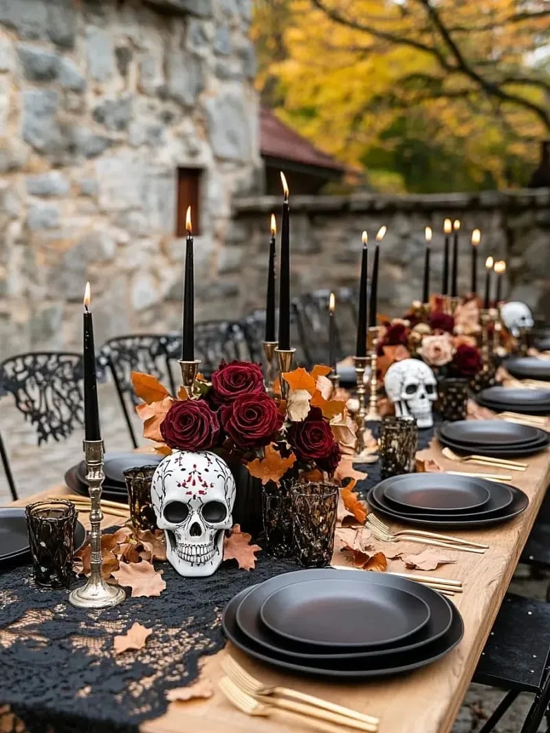 Outdoor Halloween tablescape with black plates, skulls, burgundy roses, candles, and autumn leaves
