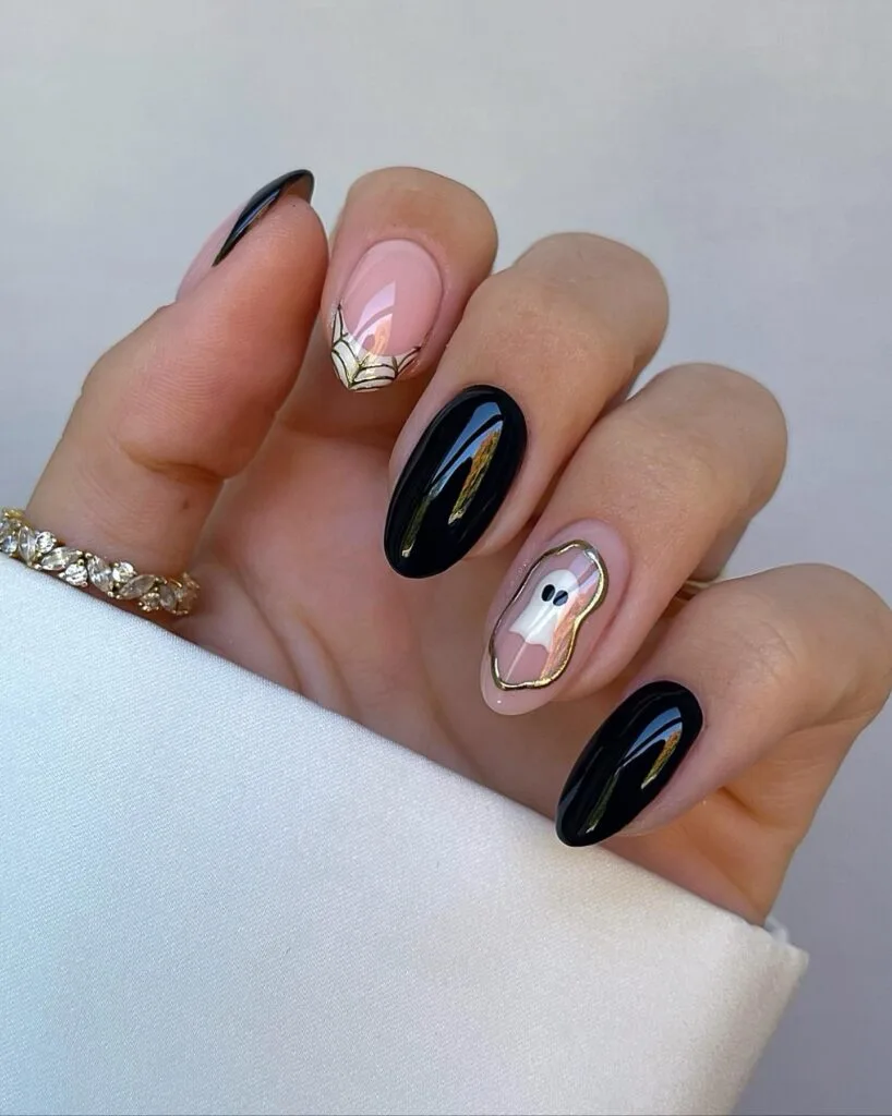 short Halloween nails with glossy black polish, a gold spiderweb accent, and a ghost framed in gold