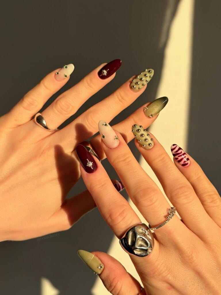October nails with sage shimmer, ivory accents, deep wine polish, silver studs, and almond shapes.