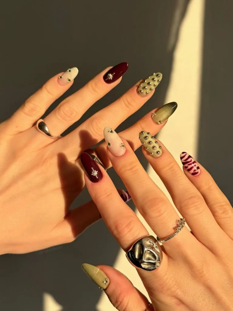 October nails with sage shimmer, ivory accents, deep wine polish, silver studs, and almond shapes.