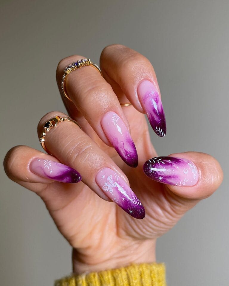 Pink and purple marbled witchy nails with white moths, leafy sprigs, moons, and stars on long almond shapes.