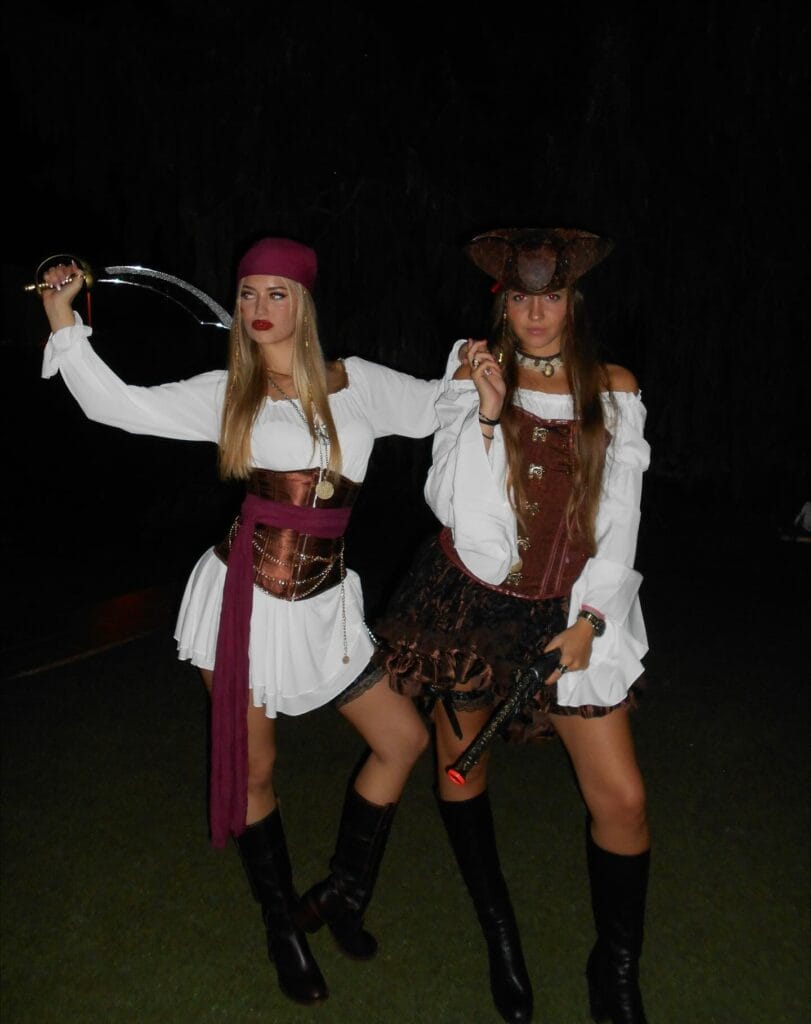 Best friend pirate costumes with white puff sleeves, brown corsets, a burgundy sash, a tricorn hat, and tall boots.
