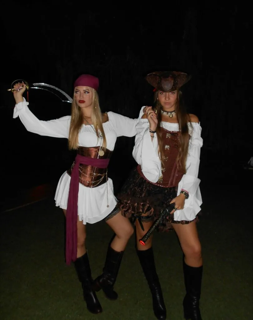 Best friend pirate costumes with white puff sleeves, brown corsets, a burgundy sash, a tricorn hat, and tall boots.