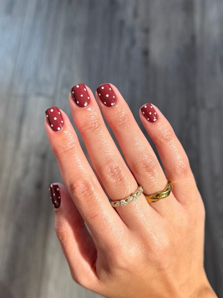 Short square autumn nails with glossy berry red polish and scattered white polka dots.
