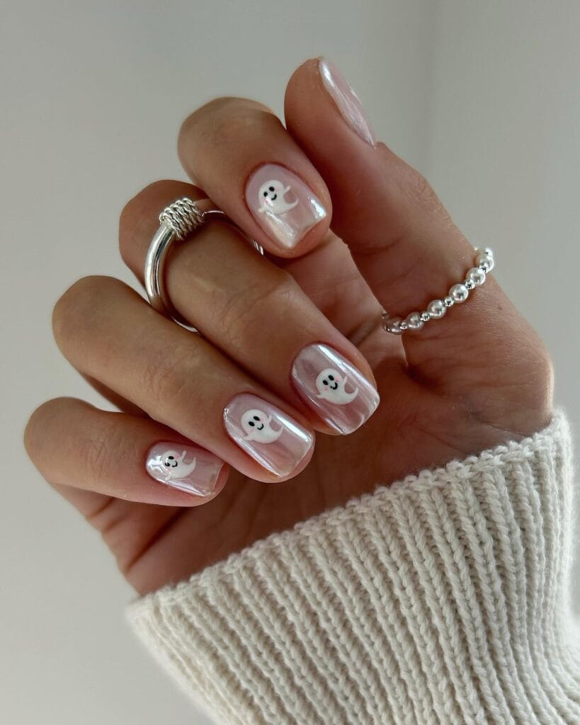 short spooky nails with pearly pink chrome polish and tiny white ghost art on each nail
