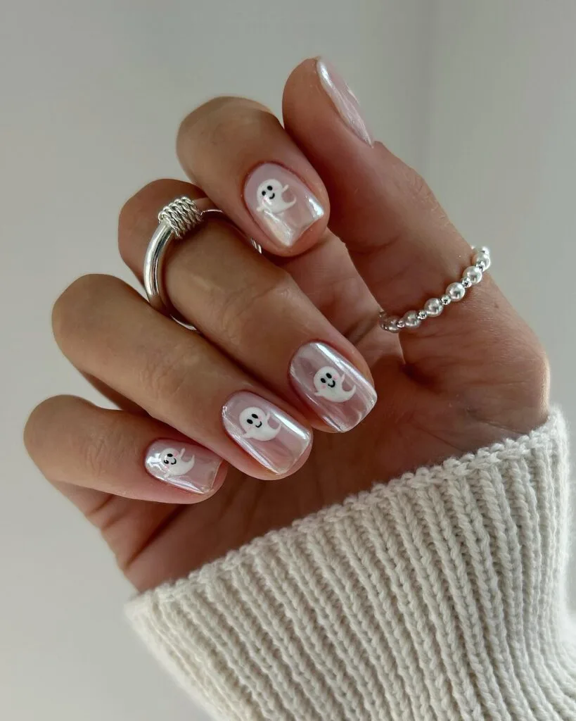 short spooky nails with pearly pink chrome polish and tiny white ghost art on each nail