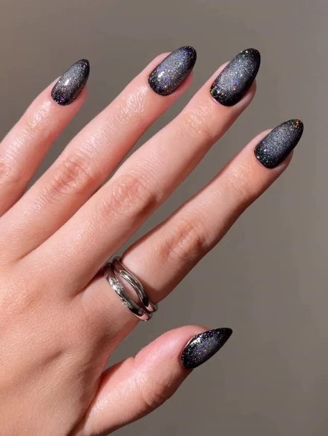 Black almond nails with dense silver and rainbow sparkle for a glittery witchy manicure.