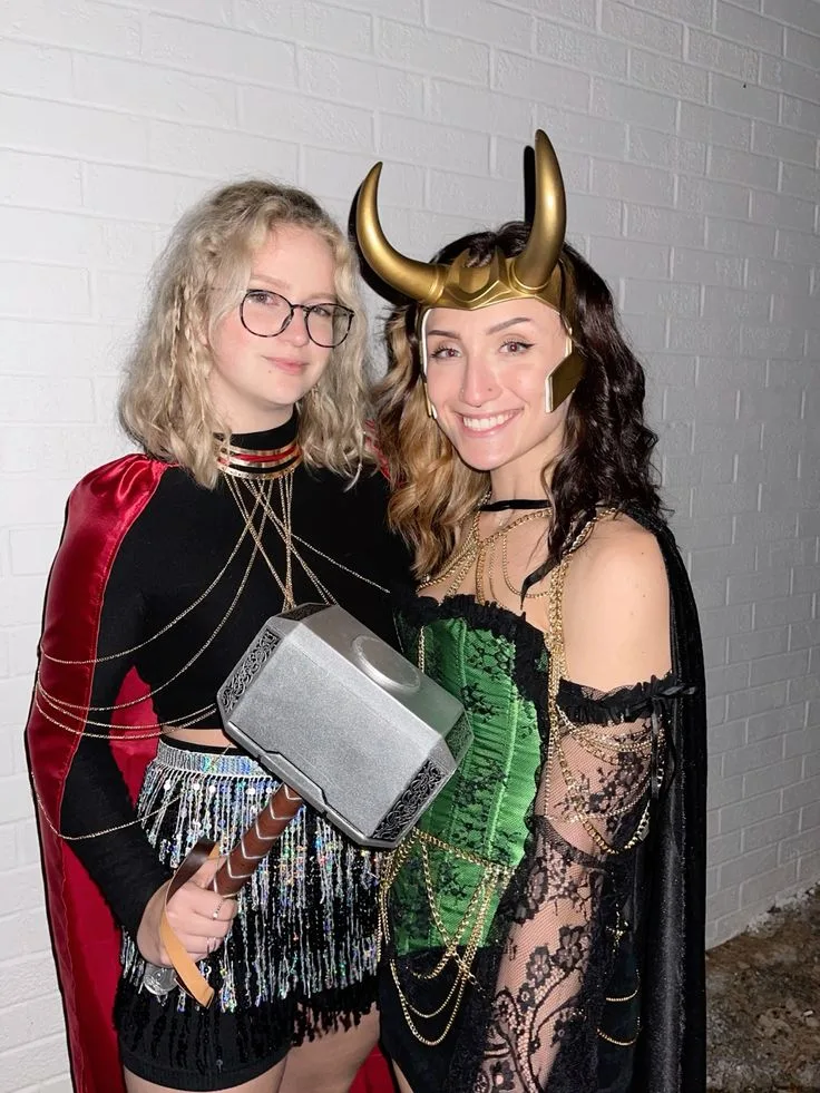 Best friend Thor and Loki costumes with a red cape, hammer, green corset, gold horns, and layered chains.